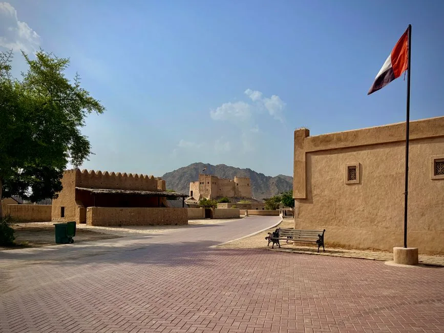 View of Fujairah Fort with scenic surroundings and UAE flag in warm daylight, showcasing Emirati architecture.
