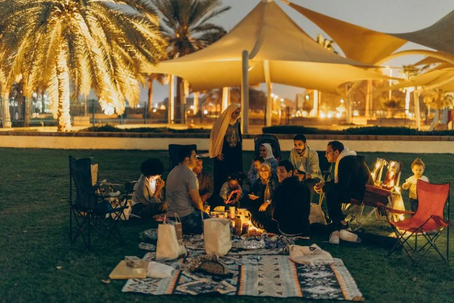 A group of people enjoying a cozy outdoor gathering under palm trees in Abu Dhabi at night.
