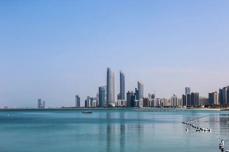 Stunning view of the Abu Dhabi skyline reflecting in the calm Gulf waters on a sunny day.