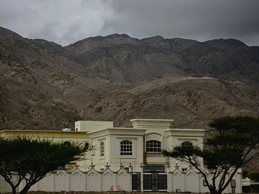 A luxurious villa set against the rugged mountains of Fujairah, UAE, under cloudy skies.